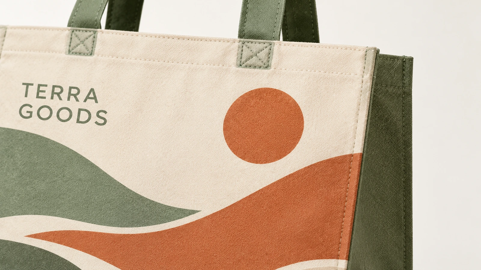 سطح حقيبة Tote المطبوع وخياطة المقبض صورة مقربة لحقيبة Tote بطباعة منظر طبيعي وكتابة TERRA GOODS ومقابض خضراء مخيطة